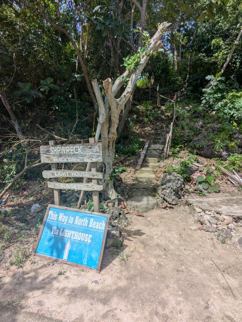 Wooden signposts directing to Shipwreck Beach and the lighthouse, with a trail leading into a lush green area.