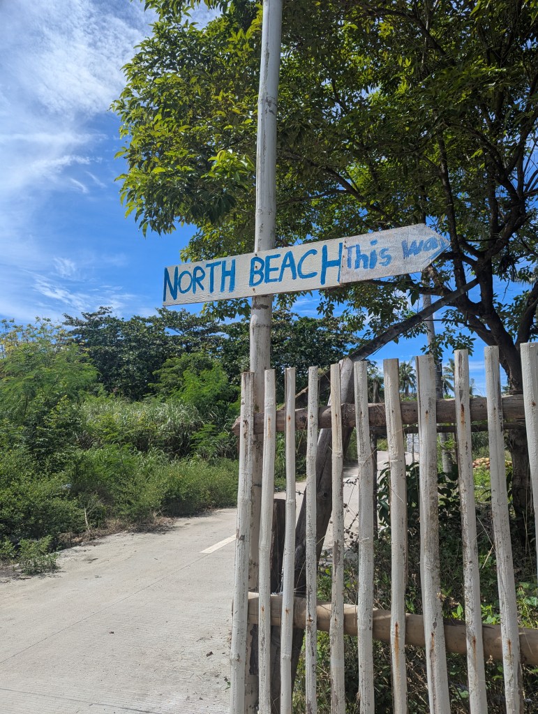 A wooden sign pointing towards 'North Beach' with a blue sky and trees in the background.