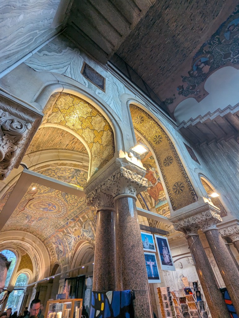 Interior view of a grand architectural space with ornate arches, detailed mosaics, and decorative columns, illuminated by soft lighting.
