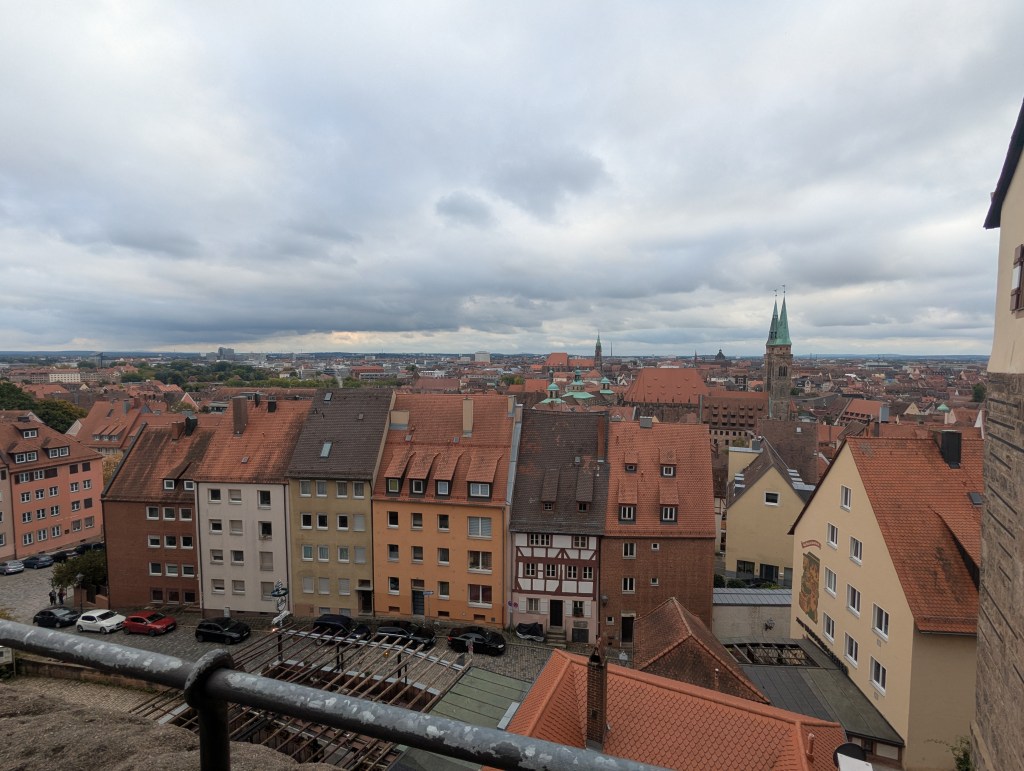 Panoramic view of a picturesque cityscape featuring houses with red roofs and a tall church steeple, under a cloudy sky.