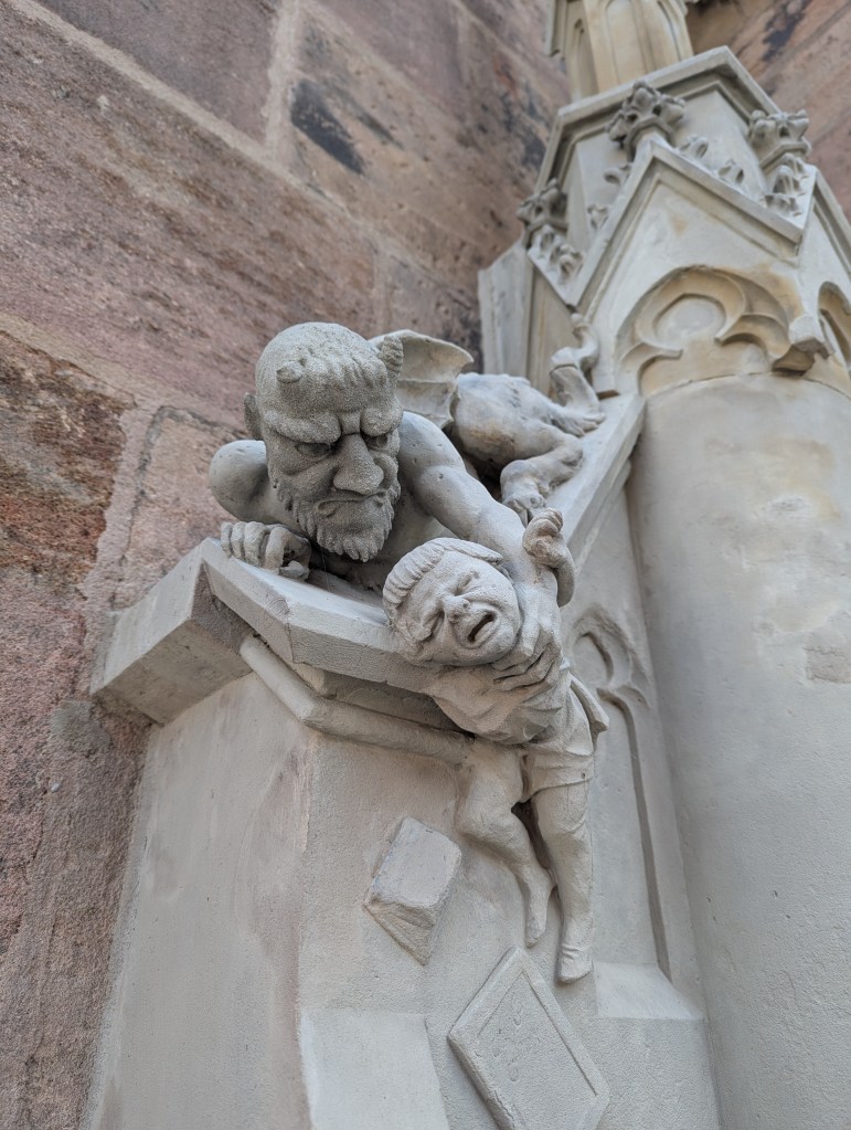 A detailed stone sculpture depicting a devilish figure holding a crying child, set against a textured wall.