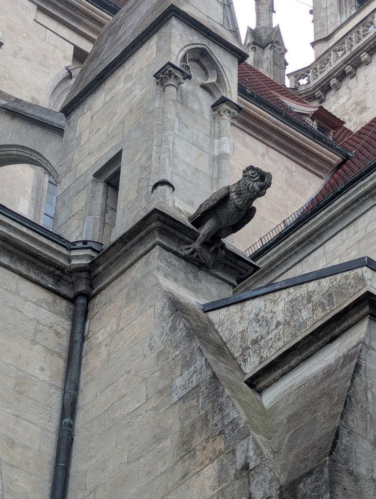 A stone carving of a gargoyle resembling an eagle perched on the edge of a Gothic-style building, showcasing intricate architectural details.