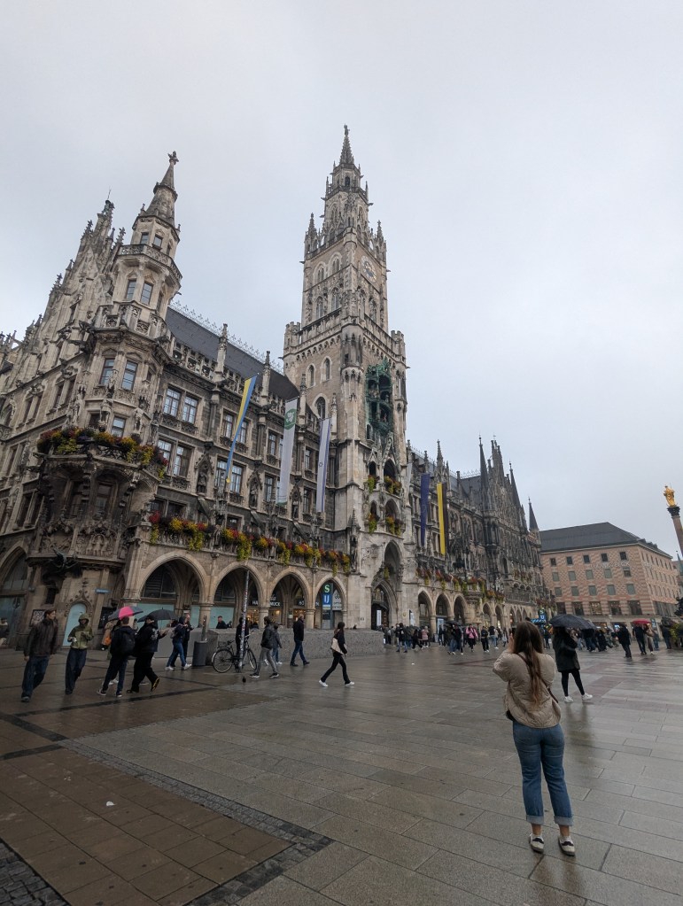 View of the Neues Rathaus (New Town Hall) in Munich with its iconic clock tower, surrounded by pedestrians on a rainy day.