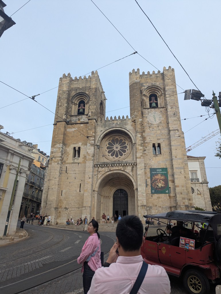 Facade of a historic cathedral with twin towers and a large rose window, surrounded by people on a cobblestone street.