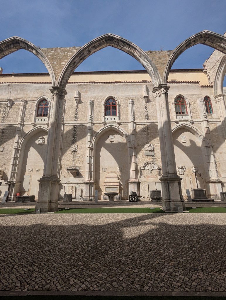 Ruins of a historic building with arched stone structures and decorative windows, set against a clear blue sky.