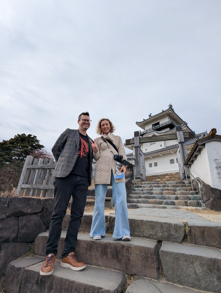 Two people standing on stone steps leading to a Japanese castle, smiling and posing for the photo.
