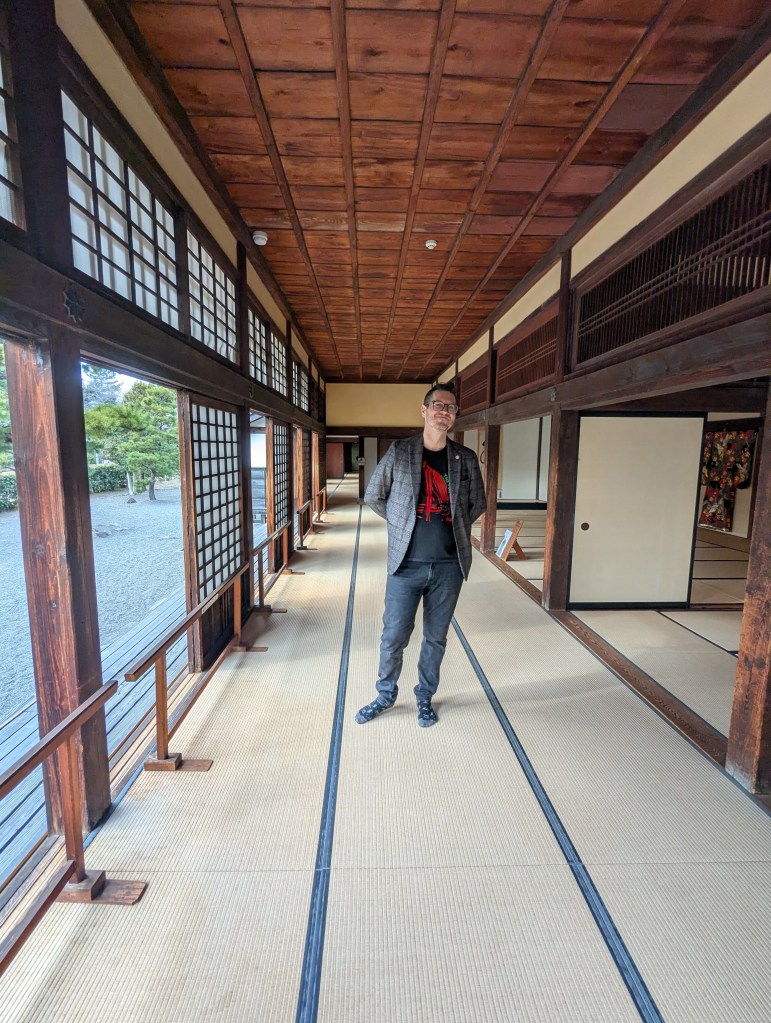 A man standing in a traditional Japanese interior hallway with wooden beams and tatami flooring.