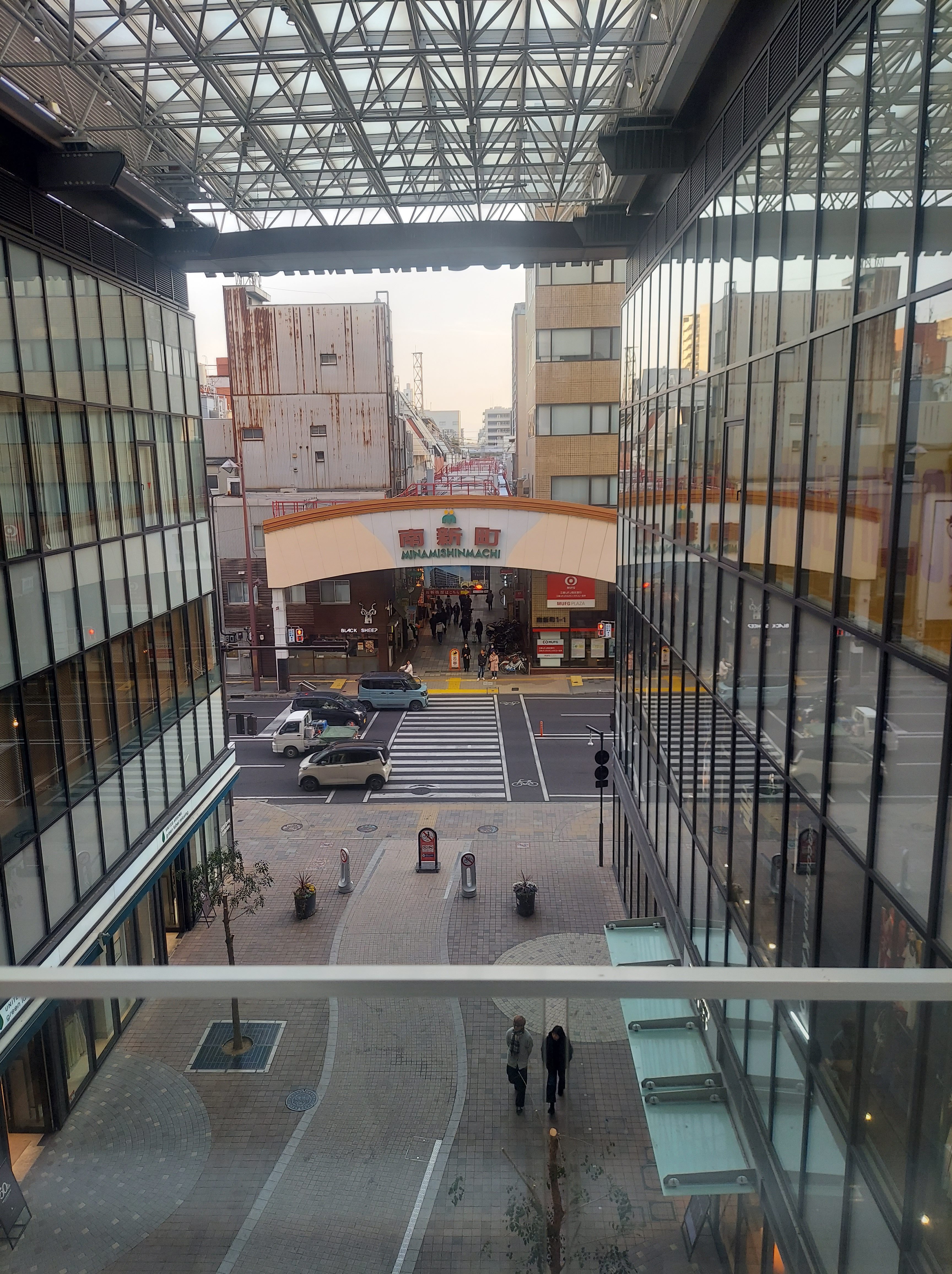View of a shopping street with a large sign reading 'MINAMISHINMACHI', surrounded by modern buildings and a busy pedestrian area.