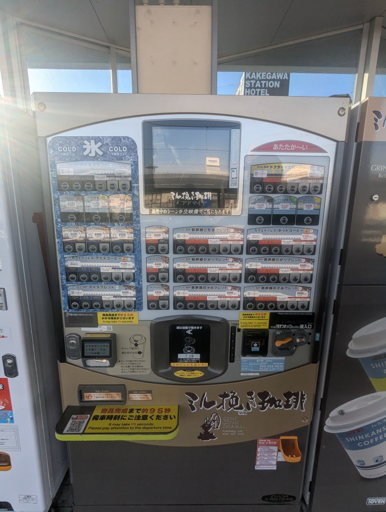 A vending machine displaying various beverage options, including hot and cold drinks, located near Kakegawa Station Hotel.